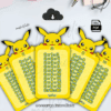 Cinco tablas de multiplicar amarillas de temática Pokémon con Pikachu se muestran en una disposición de abanico sobre un escritorio blanco con artículos de papelería. Cada tarjeta muestra una tabla de multiplicar del 1 al 10 en español.