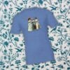 Paquete de imágenes de clipart de mujeres victorianas 9 Una camiseta azul con un estampado de tres mujeres con vestidos vintage en la espalda. El fondo presenta un estampado de flores y pájaros en azul y blanco.