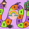 Un colorido camino de juego de mesa con temática de Halloween con espacios numerados del 1 al 15. Presenta una bruja, un murciélago, una araña y una casa encantada sobre un fondo morado. En el centro aparece un logotipo arco iris con la etiqueta 