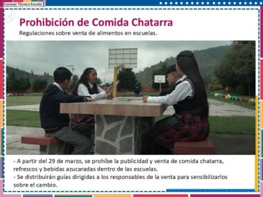 Un comedor escolar con tres estudiantes sentados en una mesa al aire libre. Un cartel encima dice "Prohibición de comida chatarra" con reglas sobre la restricción de comida chatarra, refrescos y bebidas azucaradas en las escuelas.