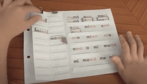 Una persona interactuando con 22 Cuadernos Dinámicos de Lectura Globalizada hechos en casa que presentan paneles doblados entrelazados etiquetados con palabras en español relacionadas con "mamá".