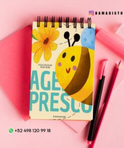 Un cuaderno de espiral con una ilustración de una abeja y una flor en la portada descansa sobre una superficie rosa, rodeado de un sobre rosa, un bolígrafo y un rotulador fluorescente. También se ven los contactos de las redes sociales y un número de WhatsApp.