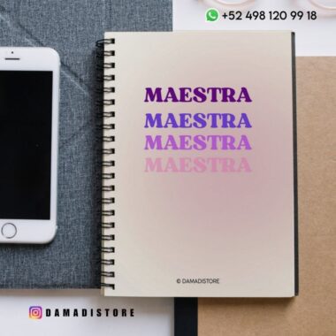 Un cuaderno de espiral con la palabra "MAESTRA" escrita cuatro veces en diferentes tonos de morado y rosa. El cuaderno está sobre un escritorio junto a un smartphone. En la imagen se ven los datos de contacto y la dirección de las redes sociales.
