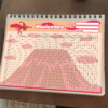 Un colorido calendario de noviembre en un cuaderno de espiral, diseñado para escolares. Tiene una ilustración de pterodáctilo rosa en la parte superior y una cuadrícula grande debajo para completar fechas y actividades. El fondo presenta un volcán estilizado y nubes en tonos rosas.