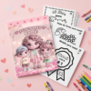 Un libro infantil para colorear con una simpática familia de dibujos animados en la portada y el texto "¡Felicidades Mamá!" se exhibe en una mesa rosa, junto a páginas para colorear, lápices de colores y corazones de papel.