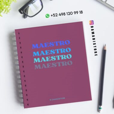 Un cuaderno de espiral con "MAESTRO" escrito cuatro veces en diferentes tonos de azul en la portada, colocado sobre un escritorio en el que se muestran gafas, un bolígrafo, una planta y la información de contacto de DAMADISTORE.