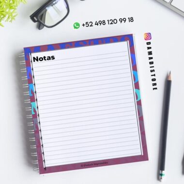Sobre un escritorio blanco, con un bolígrafo negro, gafas y una maceta cerca, hay un cuaderno de espiral abierto con una página rayada titulada "Notas". La información de contacto y la cuenta de Instagram @damadistore están visibles.