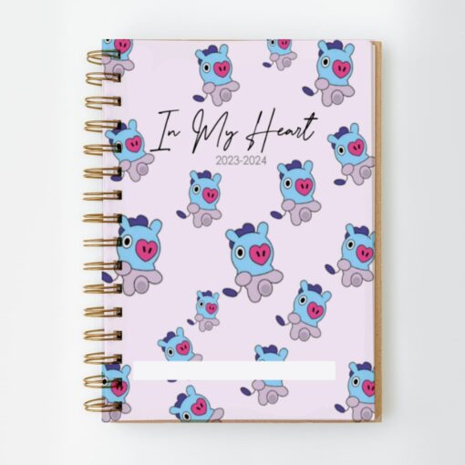 Un Cuaderno PDF encuadernado en espiral Mang BT21 BTS de 135 hojas con una cubierta rosa con lindos cerdos de dibujos animados BT21 azules y morados y el texto "In My Heart 2023-2024". El planificador tiene una sección blanca en la parte inferior para etiquetas personales.