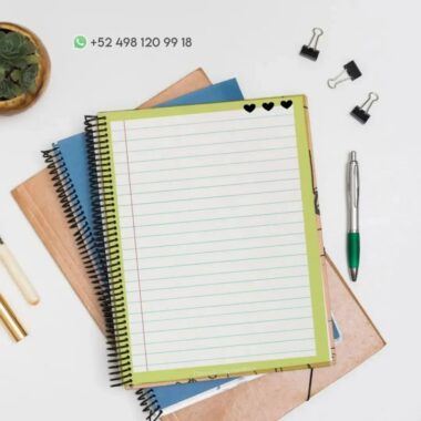 Un escritorio cuidadosamente organizado presenta un cuaderno de espiral abierto con páginas rayadas y tres íconos de corazones en la parte superior. Alrededor del PDF Cuaderno de raya Mariposa hay otros cuadernos cerrados, un bolígrafo, clips para carpetas y una planta en una maceta. Sobre los cuadernos se ve un número de WhatsApp.