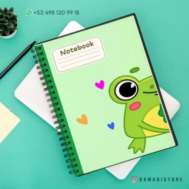 Un cuaderno de raya con diseño de rana encuadernado en espiral con una linda ilustración de rana y corazones coloridos en la portada se encuentra sobre una superficie verde. Está al lado de una pequeña maceta, un portátil blanco cerrado y un bloc de notas amarillo. Un número de contacto es visible en la parte superior y "@DAMADISTORE" está impreso en la parte inferior.