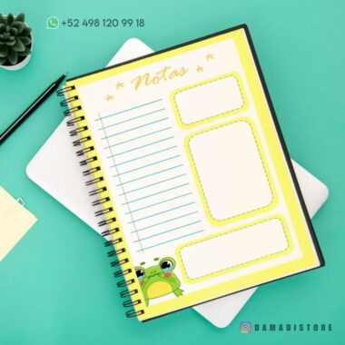 Un Cuaderno de raya con diseño de rana con secciones para notas se asienta sobre una tableta blanca sobre un fondo turquesa. También se ven una pequeña planta, notas adhesivas y un número de teléfono (+52 498 120 99 18). El cuaderno lleva la marca "Damadistore.