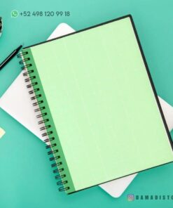 Un Cuaderno de raya con diseño de rana encuadernado en espiral se coloca sobre una superficie de color verde claro. Cerca hay un bolígrafo negro, una pequeña suculenta en una maceta y una nota adhesiva amarilla. El texto en la parte superior muestra un número de teléfono y el identificador de Instagram 