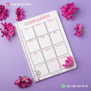 Una agenda encuadernada en espiral en color pastel 2024 descansa sobre una superficie violeta, rodeada de flores rosas. El cuaderno presenta secciones mes a mes para escribir cumpleaños y elementos de la agenda para 2024. La información de contacto de “DAMADASTORE” se muestra en la parte inferior con un número de WhatsApp.