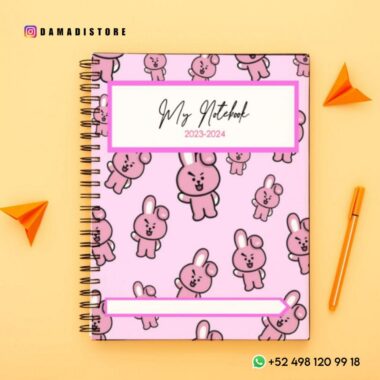 Un cuaderno de espiral rosa con un divertido estampado de conejitos y el texto "Paquete de cuadernos BT21 PDF" en la portada. El fondo es amarillo con dos aviones de papel naranja. La información de contacto se muestra en la esquina inferior derecha y un identificador de Instagram, @damadistore, con lindos personajes de BT21, está en la parte superior izquierda.