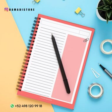Un Cuaderno BT21 VAN, encuadernado en espiral, de color rojo, abierto por una página rayada con una columna en blanco y un bolígrafo negro colocado en diagonal. Suministros de oficina como una planta, clips para carpetas, rollos de cinta adhesiva y clips rodean el cuaderno. Los datos de contacto y un identificador de redes sociales son visibles en las esquinas, lo que da a entender el encanto de BT21.
