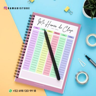 Una agenda semanal encuadernada en espiral con marco rosa titulada "Cuaderno BT21 VAN", que muestra los días de la semana en español y presenta adorables personajes de BT21. La agenda está llena de columnas de lunes a viernes, colocadas sobre una superficie azul con una planta suculenta, clips, cinta adhesiva, bolígrafos y un número de teléfono y una cuenta de Instagram.