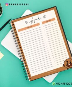 Un Cuaderno BT21 Shooky está abierto sobre un escritorio verde, con columnas para 