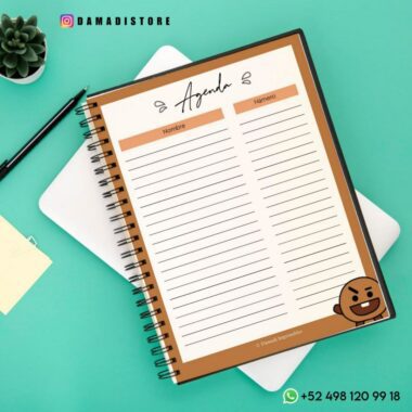 Un Cuaderno BT21 Shooky está abierto sobre un escritorio verde, con columnas para "Nombre" y "Número". Un genial personaje de dibujos animados marrón, Shooky de BT21, decora la esquina. Son visibles el identificador "DAMADISTORE" y un número de contacto con un ícono de WhatsApp. Cerca hay un bolígrafo, una planta y una carpeta abierta.