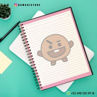 Un Cuaderno BT21 Shooky con cubierta rosa y páginas rayadas se encuentra encima de una tableta blanca. Un personaje estilizado de dibujos animados Shooky de BT21 está superpuesto en el cuaderno. A su alrededor se ven un bolígrafo negro, una pequeña planta, una nota adhesiva e información de contacto.