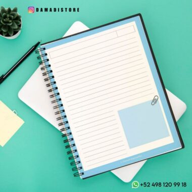 Un Cuaderno BT21 Shooky encuadernado en espiral está abierto y muestra páginas rayadas con una sección para notas. Cerca hay un bolígrafo negro, tarjetas pequeñas con Shooky de BT21 y una planta suculenta. Al fondo hay una tableta y un teléfono. La imagen incluye los datos de contacto de Instagram y WhatsApp de Dama Di Store.