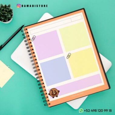 Se coloca un Cuaderno BT21 Shooky con secciones codificadas por colores sobre una superficie verde azulado. Un emoji con una cara marrón sonriente, que se parece a Shooky de BT21, adorna la sección inferior. Cerca hay un bolígrafo, una nota adhesiva y una pequeña planta suculenta. El cuaderno tiene la marca "DAMADISTORE" y un número de contacto de WhatsApp.
