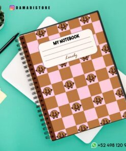 Un cuaderno de espiral sobre un escritorio con una cubierta de cuadros rosas y marrones con pequeñas ilustraciones de osos. La etiqueta de la portada dice 