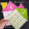 Una mano sostiene dos coloridas Casas de multiplicaciones en forma de casas, una rosa y otra verde. Estas Casa de multiplicaciones muestran problemas como 4x1, 7x1 y más. Los detalles de contacto y un identificador de redes sociales son visibles en el fondo.