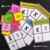 Tarjetas coloridas para aprender a multiplicar del 1 al 10 están esparcidas sobre una superficie oscura. Algunas tarjetas tienen números de colores, mientras que otras tienen tablas de multiplicar etiquetadas 