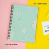 Agenda docente maestra 24-25 17 Un cuaderno encuadernado en espiral con una cubierta verde pastel con lunares de colores se coloca sobre un fondo dividido de rosa y amarillo. En la imagen se muestran el identificador de Instagram de Dameat Store y un número de WhatsApp. Cerca hay una hoja de papel con texto parcial.