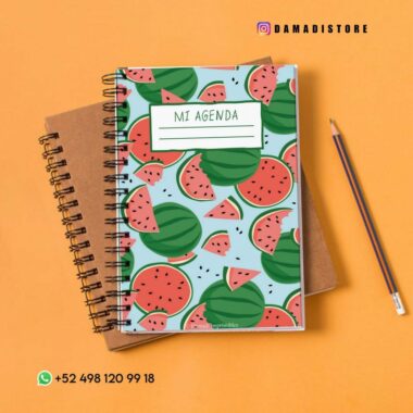 Diarios encuadernados en espiral sobre una superficie naranja, el superior con un diseño de sandía y la etiqueta "Mi Agenda". A la derecha hay un lápiz, mientras que en la esquina superior derecha está el identificador de Instagram @damadistore. La parte inferior izquierda muestra un número de contacto de WhatsApp.