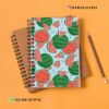 Un colorido cuaderno de espiral con un patrón de sandía en la cubierta se coloca encima de un cuaderno de espiral marrón. A la derecha hay un lápiz afilado. El fondo es una superficie suave, cálida y de color naranja. La imagen incluye información de contacto y identificadores de redes sociales.