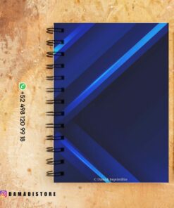 Un cuaderno de espiral azul con líneas geométricas se asienta sobre una superficie de color marrón claro. Hay un lápiz a la derecha del cuaderno. Hay datos de contacto e información de marca al lado del cuaderno. El identificador de Instagram @DAMADISTORE es visible en la esquina inferior izquierda.
