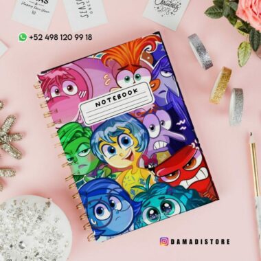 Cubierta de cuaderno con coloridos personajes animados, cada uno de los cuales expresa diferentes emociones. El cuaderno se encuentra sobre una superficie blanca, cerca de elementos decorativos como cintas, una maceta y un adorno de cristal. La información de contacto y un identificador de redes sociales se muestran arriba.