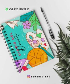 Un cuaderno encuadernado en espiral con una cubierta colorida con divertidas ilustraciones, que incluyen una pelota de baloncesto, una paleta de pintura, un avión de papel y flores. En la portada aparece el título 
