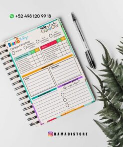 Una vista superior de una colorida agenda encuadernada en espiral abierta sobre una superficie blanca con una planta de helecho verde cerca. El planificador tiene secciones para metas, compromisos, afirmaciones positivas, actividades y reflexiones. Al lado se coloca un bolígrafo negro. También hay información de contacto y un identificador de Instagram en la parte inferior.