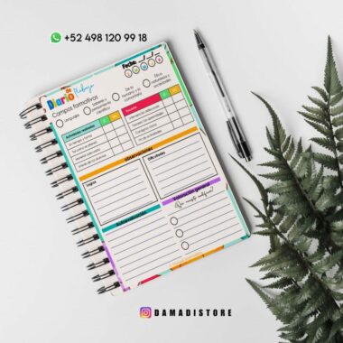 Una vista superior de una colorida agenda encuadernada en espiral abierta sobre una superficie blanca con una planta de helecho verde cerca. El planificador tiene secciones para metas, compromisos, afirmaciones positivas, actividades y reflexiones. Al lado se coloca un bolígrafo negro. También hay información de contacto y un identificador de Instagram en la parte inferior.