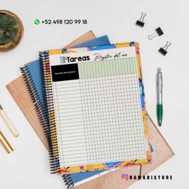 Una vista aérea de un cuaderno de espiral con una cubierta colorida sobre un escritorio. El cuaderno tiene una página titulada "Tareas Registro del mes" con columnas para los nombres de los estudiantes y las tareas. Cerca hay una planta en una maceta, un bolígrafo, un lápiz, un sujetapapeles de madera y algunos clips para carpetas.