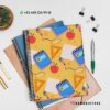 Una pila de libretas coloridas con un divertido diseño de papelería en la parte superior, que incluye elementos como libretas, bolígrafos y manzanas. El fondo incluye otros suministros como dos clips para carpetas y una planta. Los datos de contacto y el identificador de redes sociales son visibles.