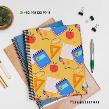 Una pila de libretas coloridas con un divertido diseño de papelería en la parte superior, que incluye elementos como libretas, bolígrafos y manzanas. El fondo incluye otros suministros como dos clips para carpetas y una planta. Los datos de contacto y el identificador de redes sociales son visibles.
