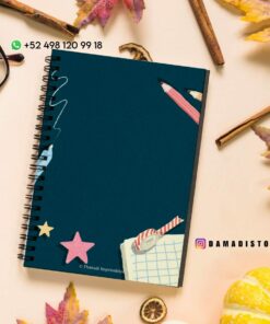 Sobre una mesa hay un cuaderno de espiral con tapa azul oscuro, rodeado de hojas de otoño, un par de vasos y una pequeña calabaza. La portada presenta recortes coloridos de estrellas, un clip, un lápiz y una hoja de papel cuadriculado. Los datos de contacto están en la esquina.