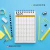 Un escritorio azul con un calendario de espiral abierto hasta agosto. Alrededor del calendario hay varios artículos de papelería amarillos y negros, como lápices, un bolígrafo, clips y notas adhesivas. La información de contacto y una cuenta de Instagram están en la esquina.