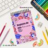 Un cuaderno titulado "Registro de mis Actividades" con coloridas ilustraciones escolares en la portada. Está colocado sobre un escritorio con lápices de colores, un sacapuntas, virutas y parte de un teclado visible. Se muestran el número de contacto y la cuenta de Instagram.