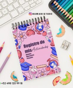 Un cuaderno titulado "Registro de mis Actividades" con coloridas ilustraciones escolares en la portada. Está colocado sobre un escritorio con lápices de colores, un sacapuntas, virutas y parte de un teclado visible. Se muestran el número de contacto y la cuenta de Instagram.