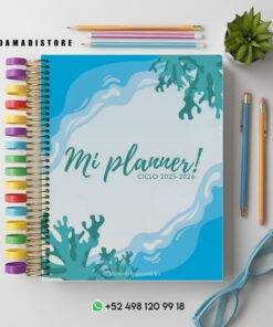 Una agenda titulada "¡Mi agenda! CICLO 2025-2026" con una portada azul océano con diseños coralinos. Pestañas de colores en el lado izquierdo. Cerca hay unas gafas, una pequeña planta verde y la información de contacto de Damadistore en la parte inferior.