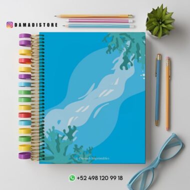 Un colorido cuaderno de espiral con una cubierta azul con temática oceánica y algas. Alrededor hay lápices de colores, gafas azules, una planta verde y la información de contacto de una tienda.