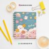 AGENDA DOCENTE PRIMARIA STAR 2025-2026 19 Un bonito cuaderno en tonos pastel con nubes, estrellas y un planeta en la portada reposa sobre un escritorio blanco con papelería amarilla, cinta adhesiva, un lápiz, clips y una taza de café. También se ven la información de contacto y las redes sociales.