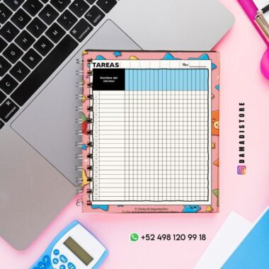Un colorido cuaderno de tareas con cuadrícula reposa sobre el teclado de una laptop. Cerca hay un bolígrafo rosa, una calculadora y una regla. Se ven el perfil de Instagram y el contacto de WhatsApp de DAMADISTORE.
