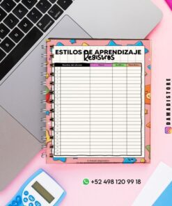 Un cuaderno espiral con una hoja de registro de estilos de aprendizaje en español se encuentra sobre un escritorio rosa, junto a una computadora portátil, una calculadora azul y un bolígrafo. La hoja tiene columnas etiquetadas como Visual, Auditiva y Kinestésica.