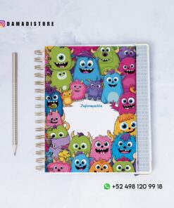 Un cuaderno de espiral con una cubierta colorida que representa monstruos sonrientes de dibujos animados, junto a un lápiz sobre una superficie blanca. El cuaderno dice 