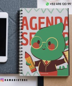 Un cuaderno encuadernado en espiral con un simpático personaje verde de dibujos animados que sostiene un lápiz y una regla en la portada, junto a un smartphone y un papel. En la imagen aparece "DAMADISTORE" y la información de contacto.
